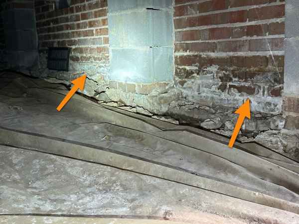 White, crusty salt deposits along the base of a brick crawl space wall, marked with orange arrows