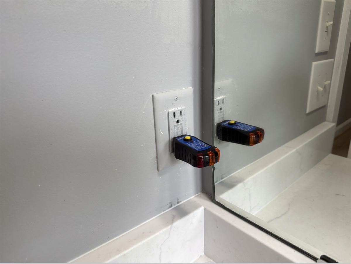 A GFCI tester plugged into a bathroom outlet beside a mirror