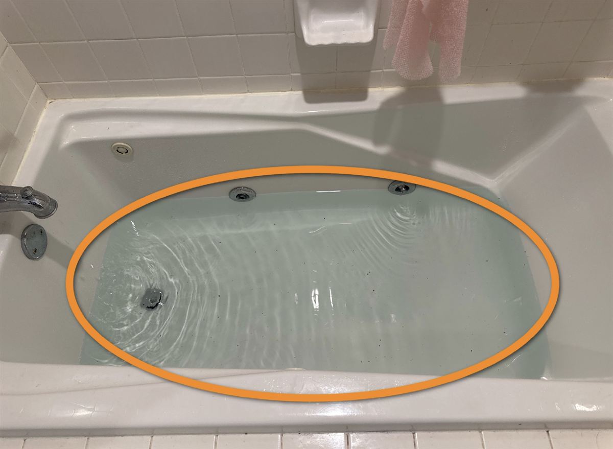 A bathtub holding water that is draining slowly, circled in orange